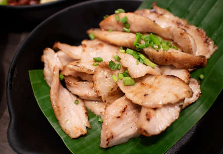 Charcoal-boiled pork neck, serving on banana leaf and black ceramic plate. Ready to eat in restaurant. North-east Thai traditional foodの写真素材