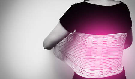 Woman in black t-shirt wearing back support belt for back pain and spinal support with red spot on her back. Medical care conceptの写真素材