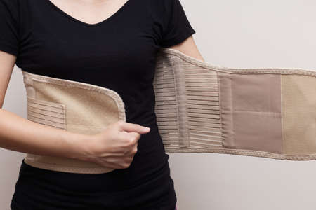 Woman in black t-shirt wearing back support belt for back pain and spinal support. Medical care conceptの写真素材