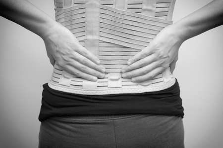 Woman in black t-shirt wearing back support belt for back pain and spinal support. black and white tone. Medical care conceptの写真素材