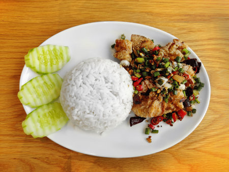 Cooked rice serving with fried fish with garlic and pepper, serving on round white plate.の写真素材