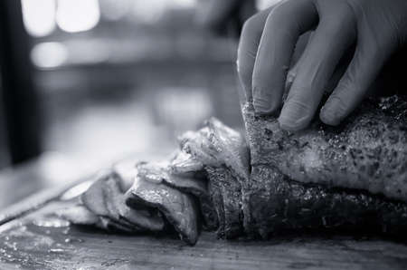 Closed up of chefâs hand slicing grilled medium rare beef steak on wooden board Barbecue. Black and white toneの写真素材