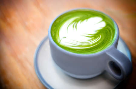 A cup of hot green tea matcha latte with beautiful latte art on wooden plate. Selective focus