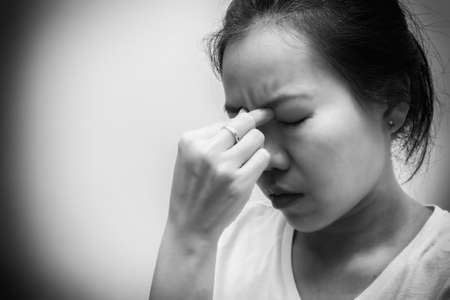 Asian woman with white t-shirt squeezes her eyebrows because headache, flu, COVID 19 or stress. Healthcare concept. Black and white toneの写真素材