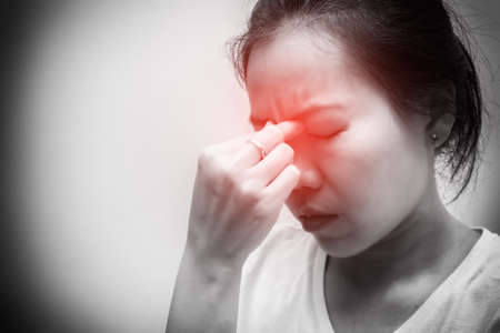 Asian woman with white t-shirt squeezes her eyebrows because headache, flu, COVID 19 or stress. Healthcare concept. Black and white tone with red spot on eyebrowの写真素材