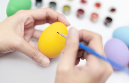 Female hands holding a paintbrush to paint the yellow eggs. Handicraft concept. Happy Easter day. Decorative concept.の写真素材