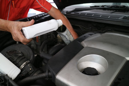 Close up hand adding fresh oil into engine car, repairing change the oil. Car maintenance at service station.の写真素材