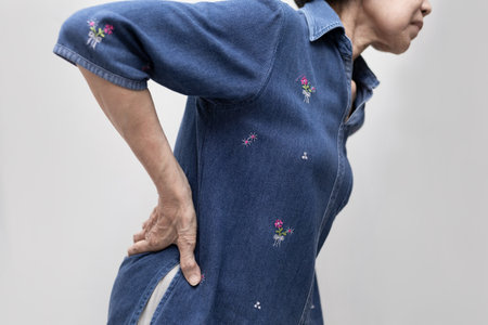 Elderly Asian woman suffering from low back pain, massaging her back to relieve pain. Geriatric society. Medical issue.の写真素材