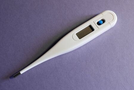 white electronic thermometer with blank screen and blue power button on violet paper background