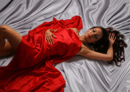 Glamour Girl lyeing on the Light background in Red Silkの写真素材