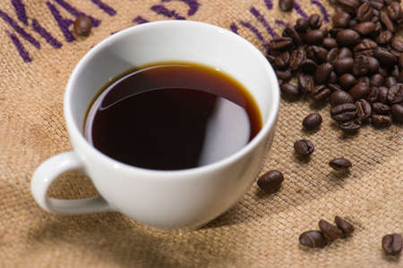 A cup of black coffee with beans on wooden table.の写真素材