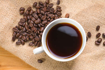 A cup of black coffee with beans on wooden table.の写真素材