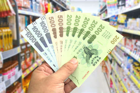 Taipei, Taiwan-Oct 11, 2021: Woman's hand hold the Quintuple Stimulus Voucher in a grocery store.のeditorial素材
