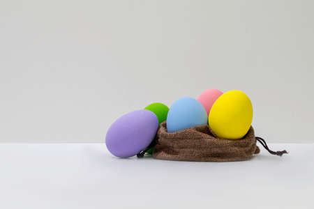 The decorated colorful easter eggs in the brown jute bag with white backgroundの写真素材