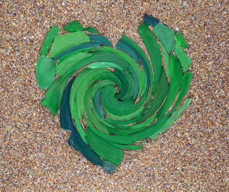 Heart symbol made of green glass on sand close-up, decorative element, twisted spiral, unusual...