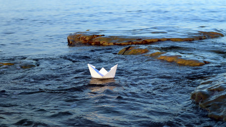 Paper boat ship floats in blue water in sea, sailboat symbol of shipping, travel concept, sailing