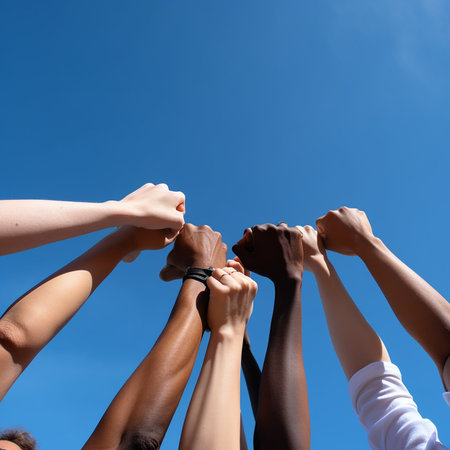 Hands with different skin colors clenched into a fist stretched up against the blue sky, the concept of solidarity, friendship, struggle, harmony, unityの素材