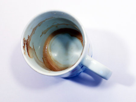 Dirty white cappuccino coffee mug with remains of brown foam on a white background close-up top view
