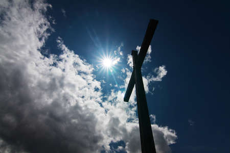 cross over blue sky with clouds againts the sunの写真素材
