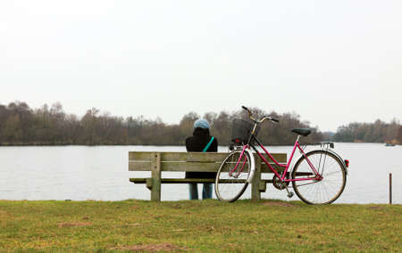 lonely girl on the bench close to the lake and bicycleの写真素材
