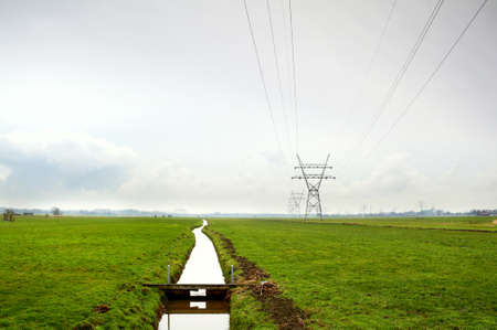 Dutch typical rural flat landscape with channel and high-voltage line の写真素材