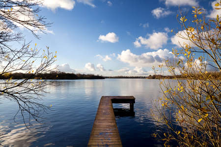 long wooden pier on lake during sunny autumn dayの写真素材