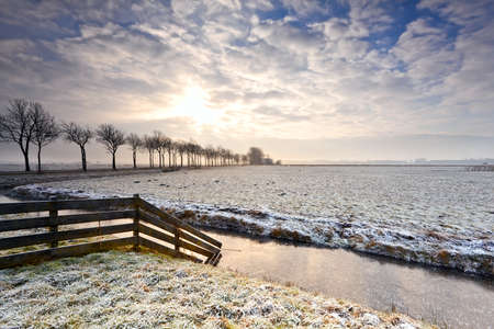 sunrise over snow pasture and canal with fenceの写真素材