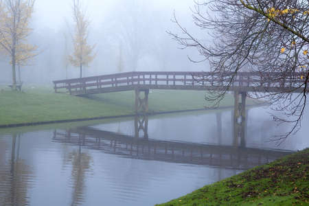 wooden bridge over river in fog during autumnの写真素材