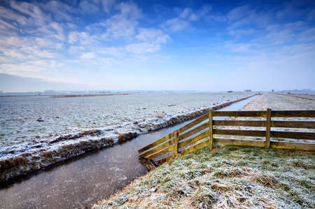 wooden fence by frozrn canal in Dutch farmlandの写真素材