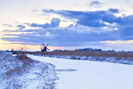 Dutch windmill by frozen river in winter at sunriseの写真素材
