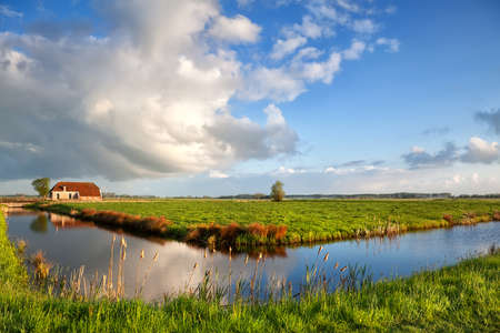 beautiful clouds over charming farmhouse and blue riverの写真素材