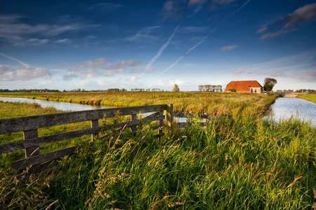 fence and farmhouse over blue sky in Dutch farmlandの写真素材