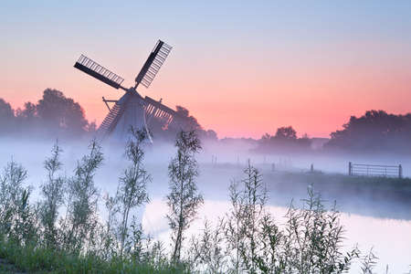 charming Dutch windmill in fog at sunriseの写真素材