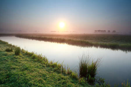 misty sunrise over river on Dutch farmland, Hollandの写真素材