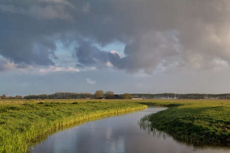 cloud sky over river in Dutch farmland, Groningen, Netherlandsの写真素材