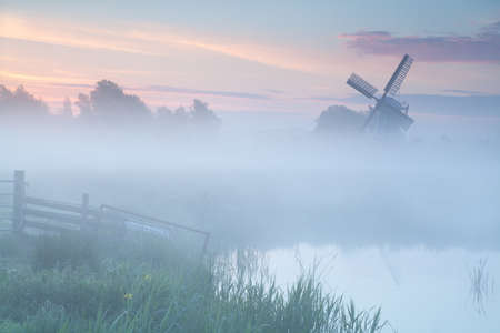 misty sunrise over Dutch windmill on farmland, Netherlandsの写真素材
