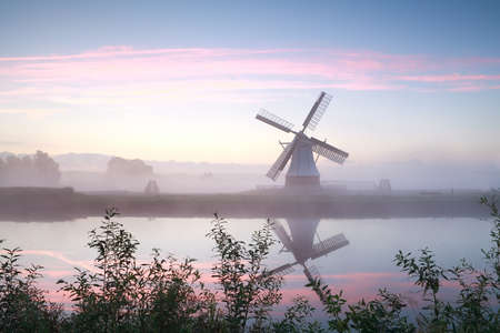 windmill by river at misty sunrise, Netherlandsの写真素材