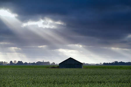 wooden hut over sky with sunbeams on farmlandのeditorial素材