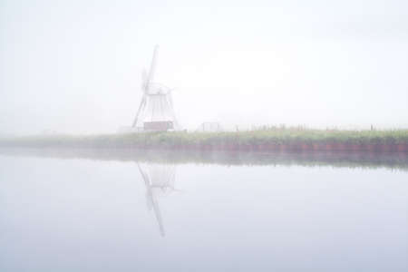 windmill reflected in river and dense fog, Netherlandsの写真素材