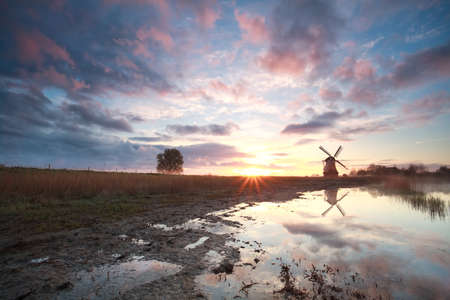 Dutch windmill at sunrise by river, Hollandの写真素材