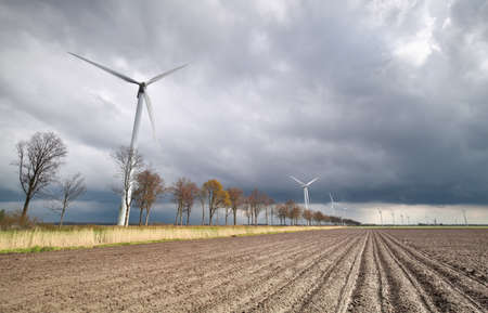 plowed potato field and windmill turbines in Dutch farmlandの写真素材