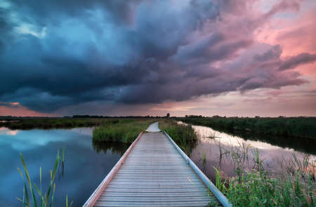 wooden path bridge over river at stormy sunset, Netherlandsの写真素材