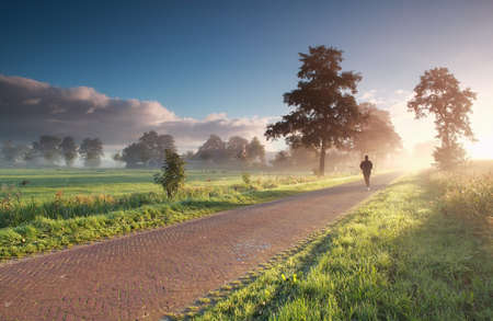 runner in countryside during misty summer sunriseの写真素材