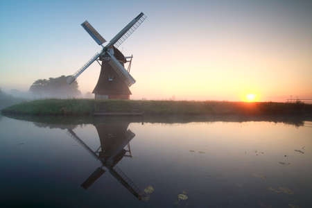 charming windmill by lake at  misty sunriseの写真素材