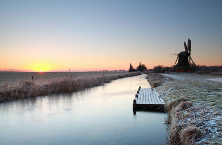 charming windmill by river at winter sunriseの写真素材
