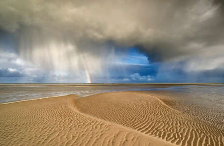 storm cloud and rainbow on sand North sea beachの写真素材