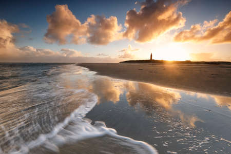 gold dramatic sunrise over lighthouse on north sea beach