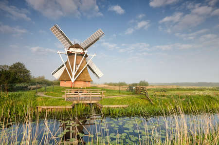 charming Dutch windmill by river over blue sky, Netherlandsの写真素材