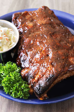 Grilled juicy barbecue pork ribs in a blue plate with coleslaw and parsley.の写真素材