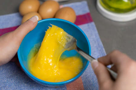 beating hens eggs in a blue bowl with a fork